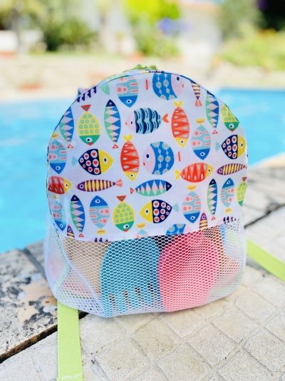 Mochila infantil branca com padrão colorido de peixes ao lado de uma piscina