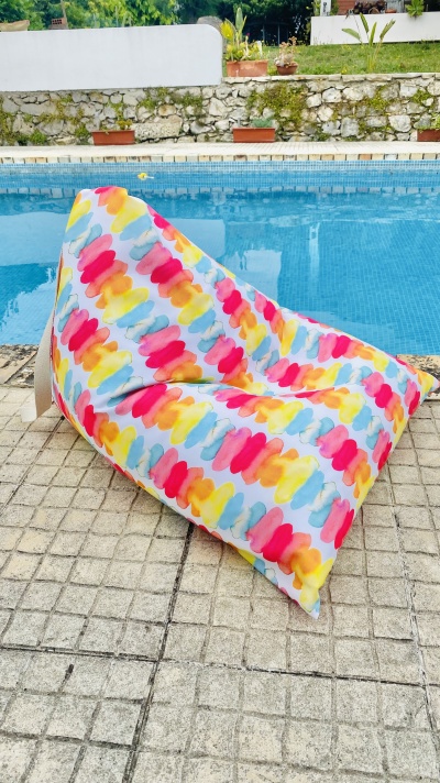 Puff colorido com padrão de pinceladas ao lado de piscina em área exterior