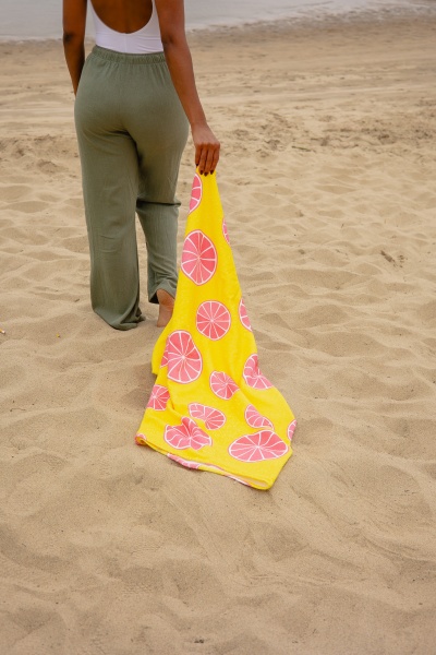 Pessoa a segurar uma toalha amarela com padrão de fatias de citrinos enquanto está na praia.