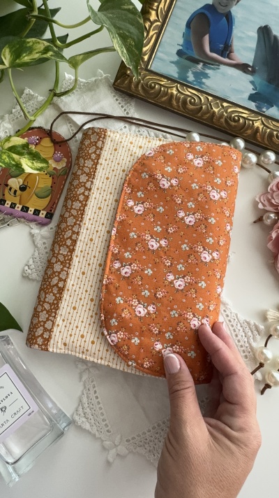Estojo e máscara de dormir floral em tecido laranja sobre toalha branca com foto em moldura dourada ao lado