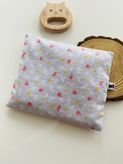 Almofada decorativa com padrão floral ao lado de mordedor de madeira em forma de gato e disco de madeira