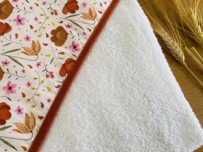 Toalha de banho branca com padrão floral colorido e borda laranja ao lado de espigas