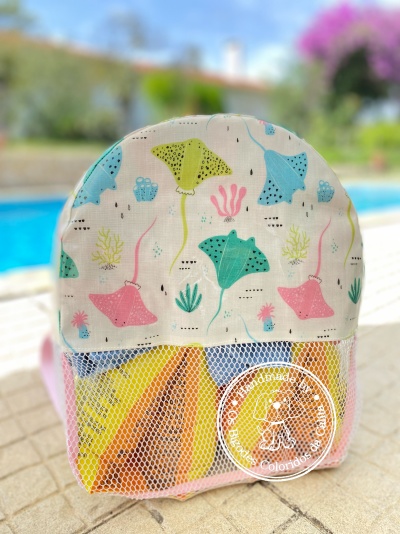 Mochila infantil colorida com padrão de raias-manta em fundo branco junto a piscina