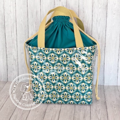 Bolsa com padrão geométrico azul e amarelo, alças amarelas e fecho de cordão verde azulado