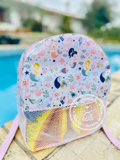 Mochila infantil cor-de-rosa com padrão de sereias e bolso em rede junto a piscina