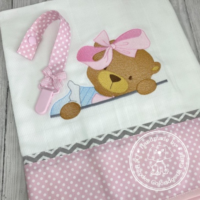 Toalha branca com ursinho bordado, faixa rosa com bolinhas e prendedor de chupeta rosa.