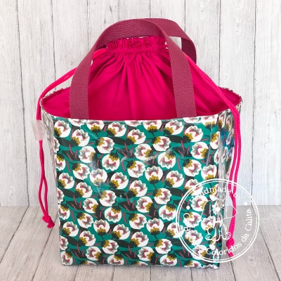 Bolsa florida com alças bordô e fecho de cordão rosa sobre superfície de madeira clara.