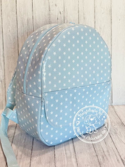 Mochila azul clara com estrelas brancas e selo handmade em fundo de madeira clara