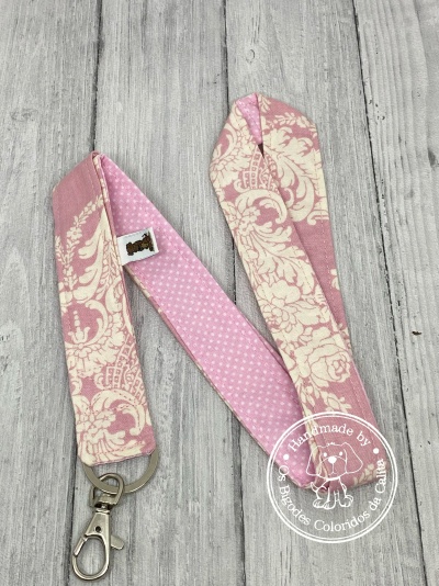 Cordão rosa com padrão floral e de pontos, com argola metálica prateada, sobre fundo de madeira cinza