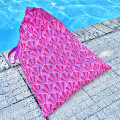Almofada triangular rosa com padrão rosa e vermelho ao lado de piscina