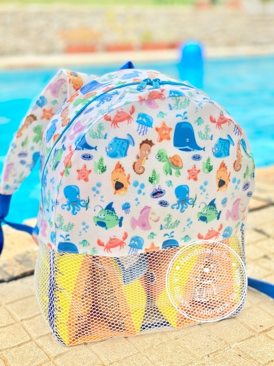 Mochila infantil colorida com animais marinhos ao lado de uma piscina