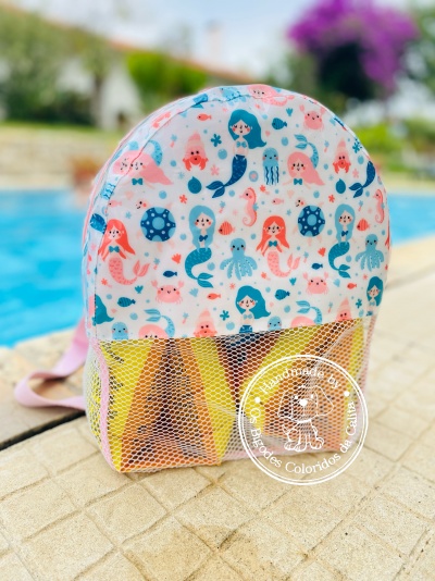 Mochila infantil colorida com padrão de sereias e bolso em rede junto a piscina