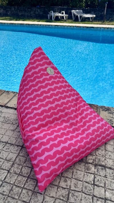Pufe rosa triangular com padrão ondulado junto a piscina azul