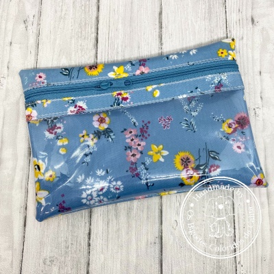 Bolsa pequena azul com padrão floral colorido e fecho de correr colocada sobre madeira clara