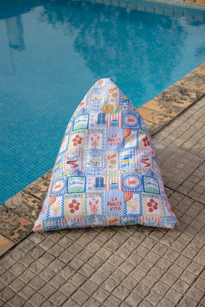 Puff triangular colorido junto à piscina com padrão de azulejos e textos em inglês e italiano.