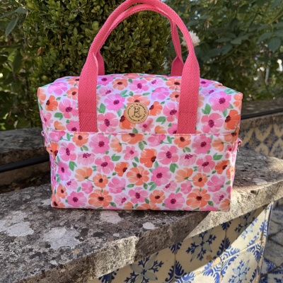 Mala floral colorida com alças rosa e etiqueta de madeira em ambiente exterior