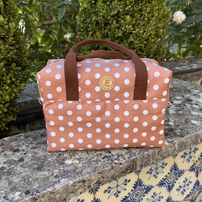 Bolsa de tecido castanha com bolinhas brancas e alças castanhas sobre muro de pedra com azulejos