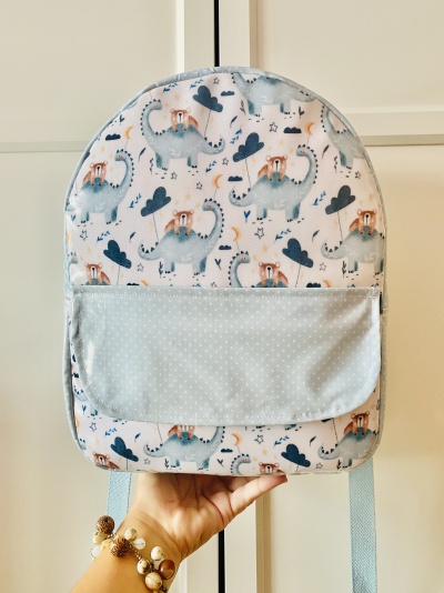 Mochila infantil com padrão de dinossauros e bolso cinza claro com pontos brancos