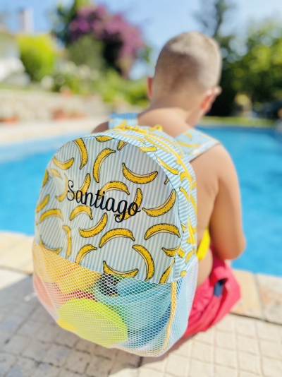 Mochila azul clara com bananas amarelas e nome Santiago junto a piscina
