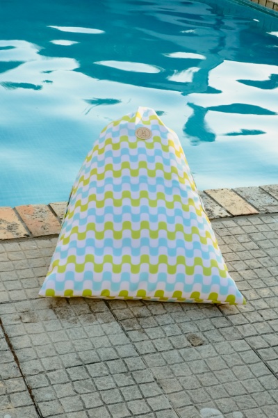 Pufe de tecido com padrão colorido junto a piscina azul com pavimento em mosaico cinzento e tijolos