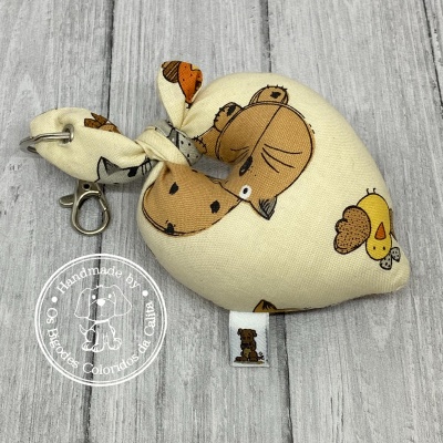 Mini saco de tecido com desenhos de animais em tons castanho, bege e amarelo, com argola metálica