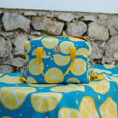 Bolsa pequena azul com padrão de limões amarelos e alças amarelas sobre tecido com padrão de limões