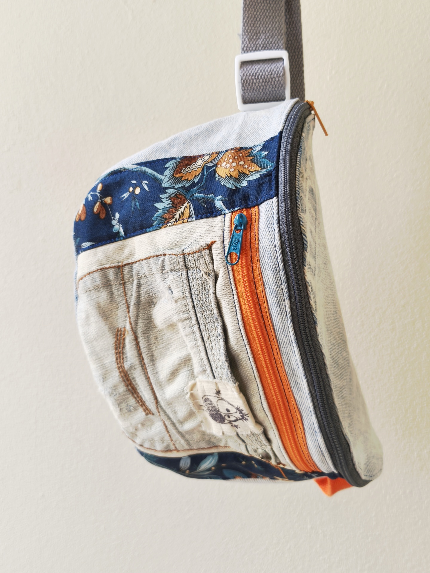 Bolsa de cintura Os básicos! Mala tipo sling com tecido claro, detalhes florais azuis e zíperes laranja e cinza