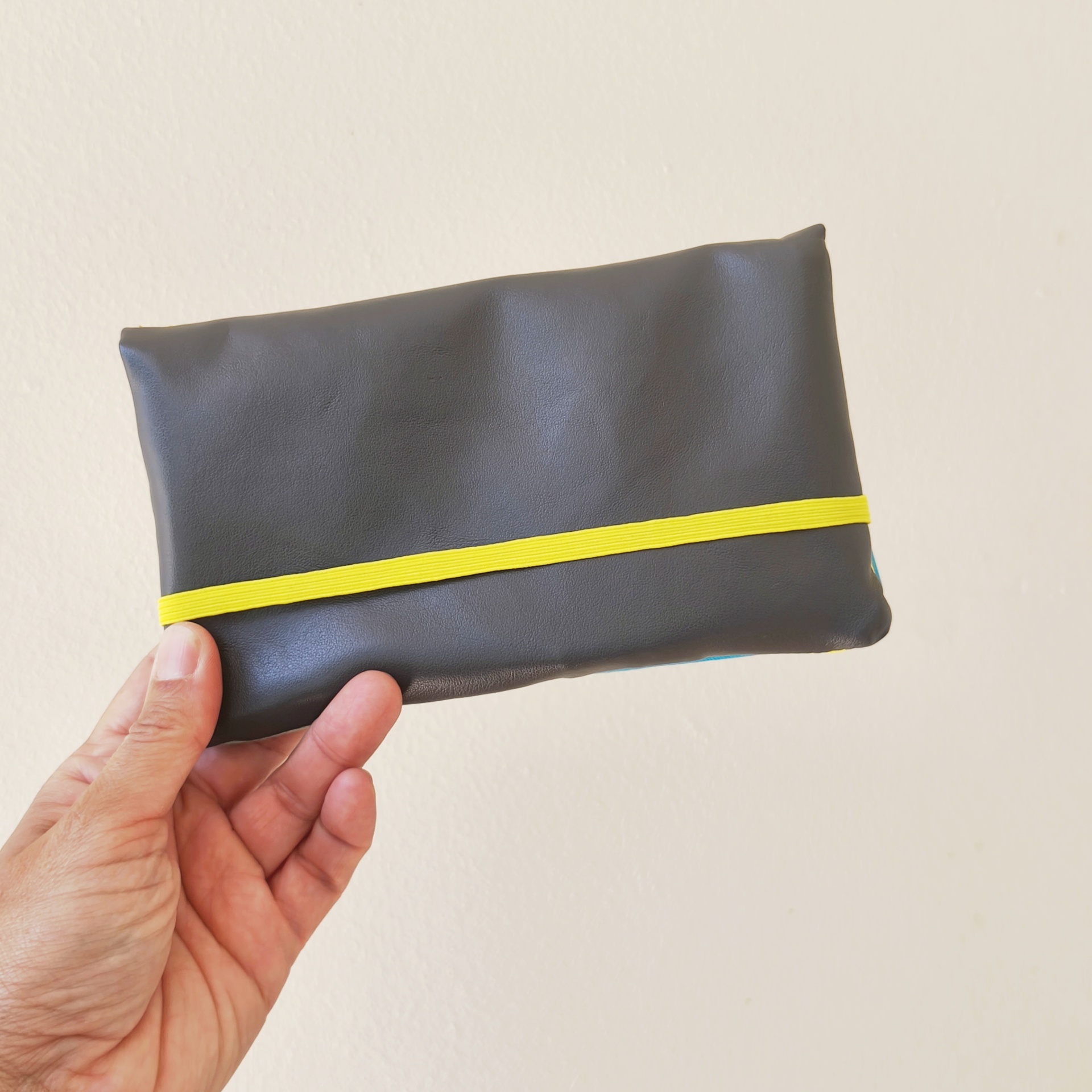 Carteiras porta-tudo! Mala pequena preta com faixa amarela sendo segurada por uma mão