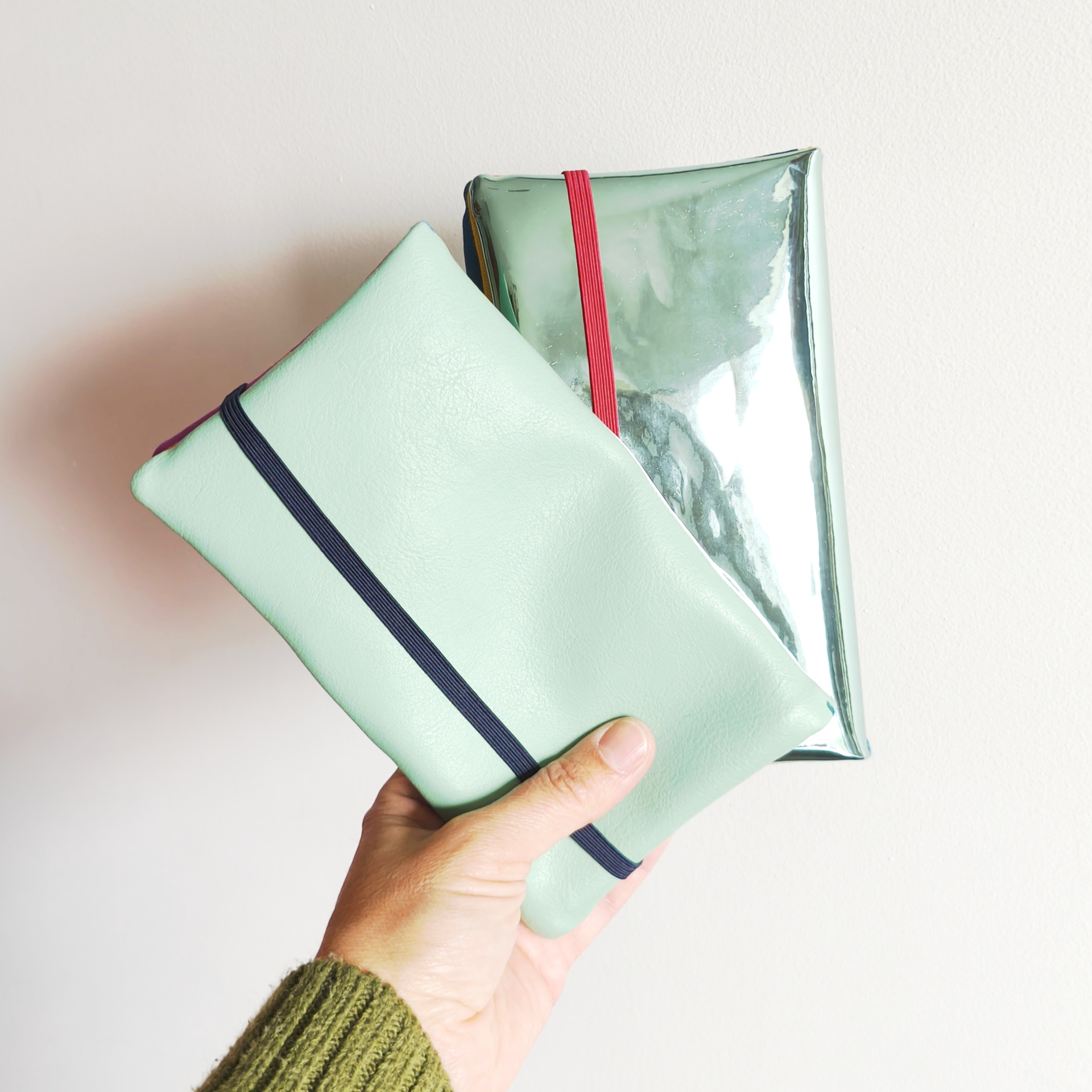 Carteiras porta-tudo! Duas bolsas retangulares, verde claro e prateada, seguradas por mão