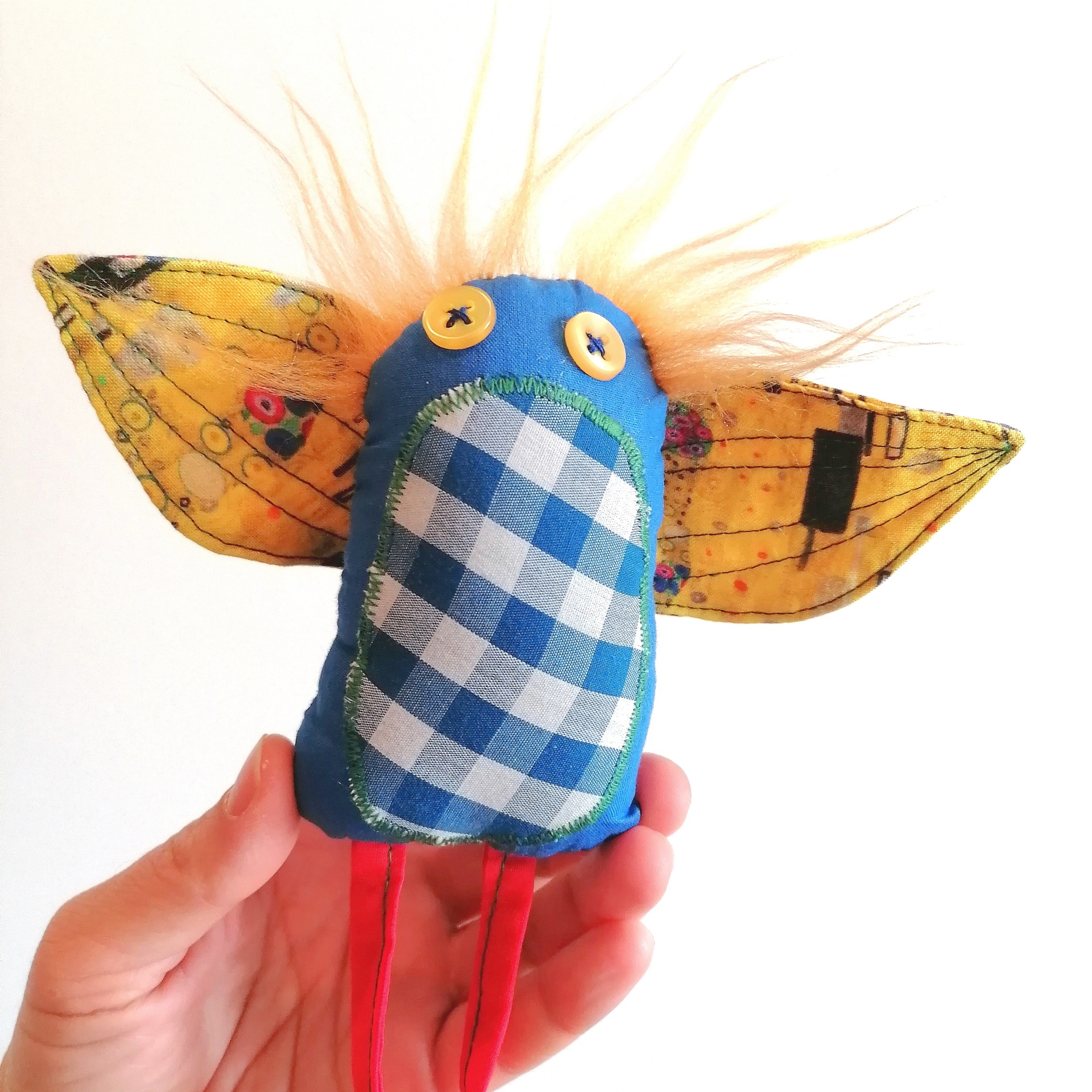 Passatortos! Boneco artesanal colorido em tecido com orelhas grandes e cabelo laranja, segurado por mão.