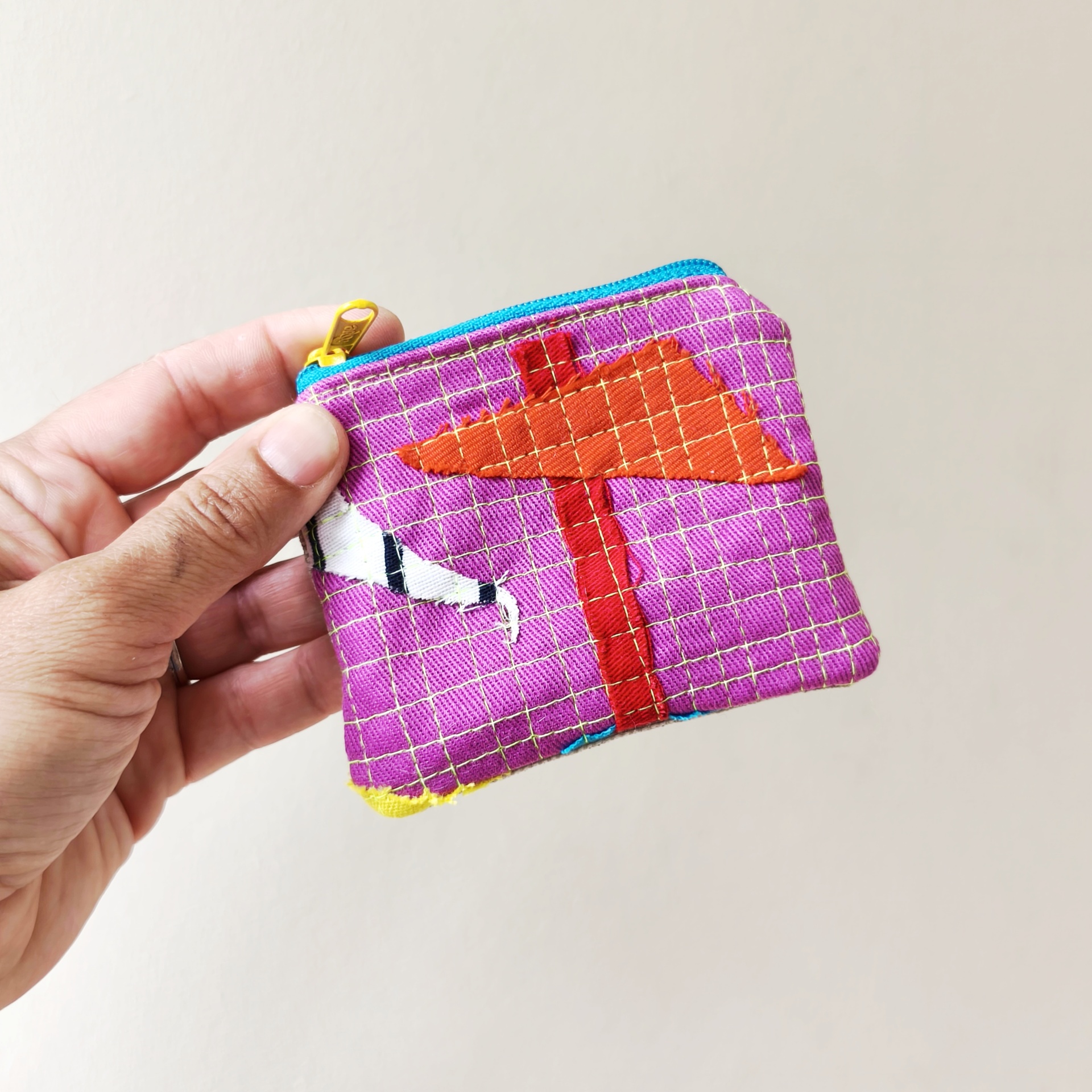 Mini bolsa trapo Carteira roxa com padrão dourado e bordado laranja de árvore, fecho de correr azul e puxador amarelo na mão.