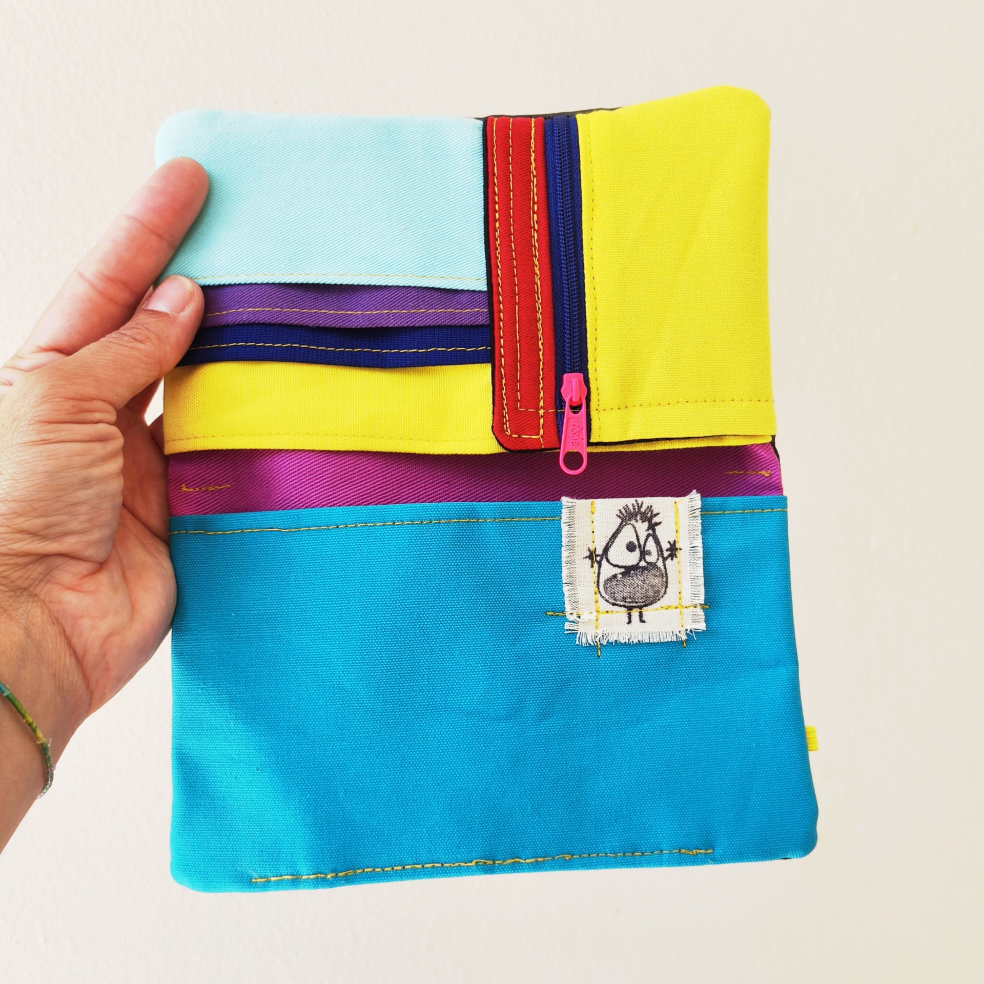 Carteiras porta-tudo! Carteira ou estojo multicolorido em tecido com zíper cor-de-rosa e etiqueta com desenho de rosto.