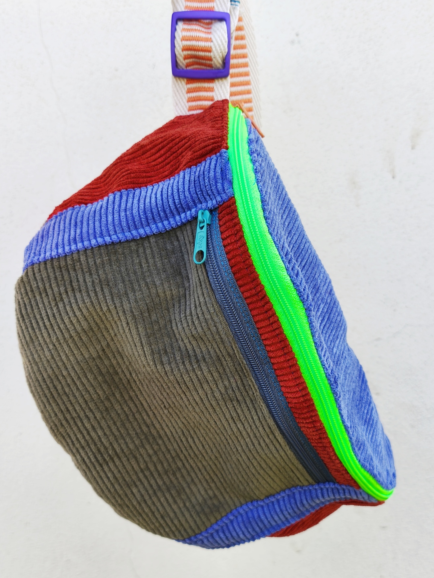 Bolsa de cintura BOMBAzine! Mochila colorida em tecido de veludo cotelê com alça branca listrada suspensa numa parede branca