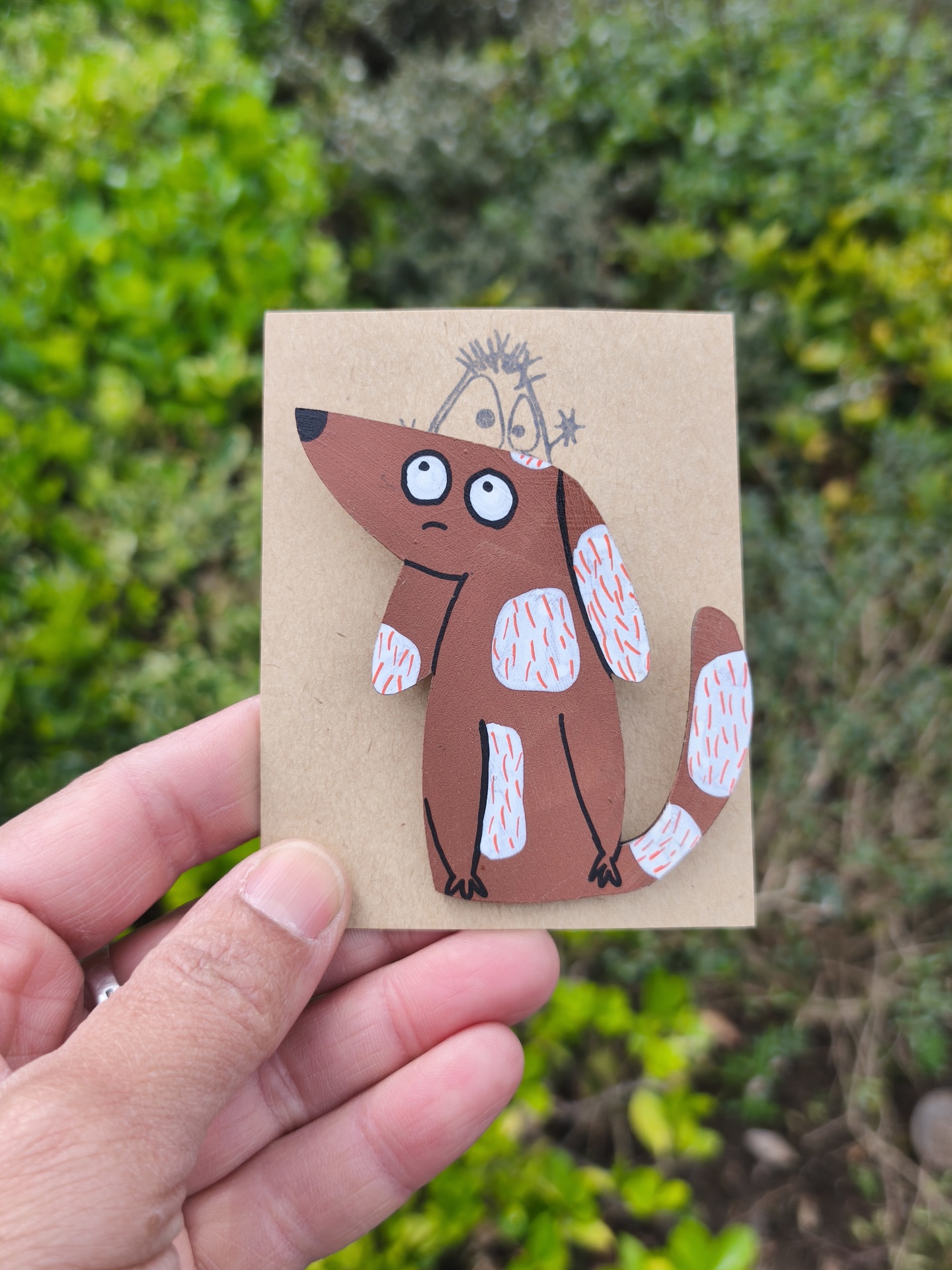 Alfinete cão! Broche de cão castanho com manchas brancas e pêlos vermelhos, sobre cartão castanho.