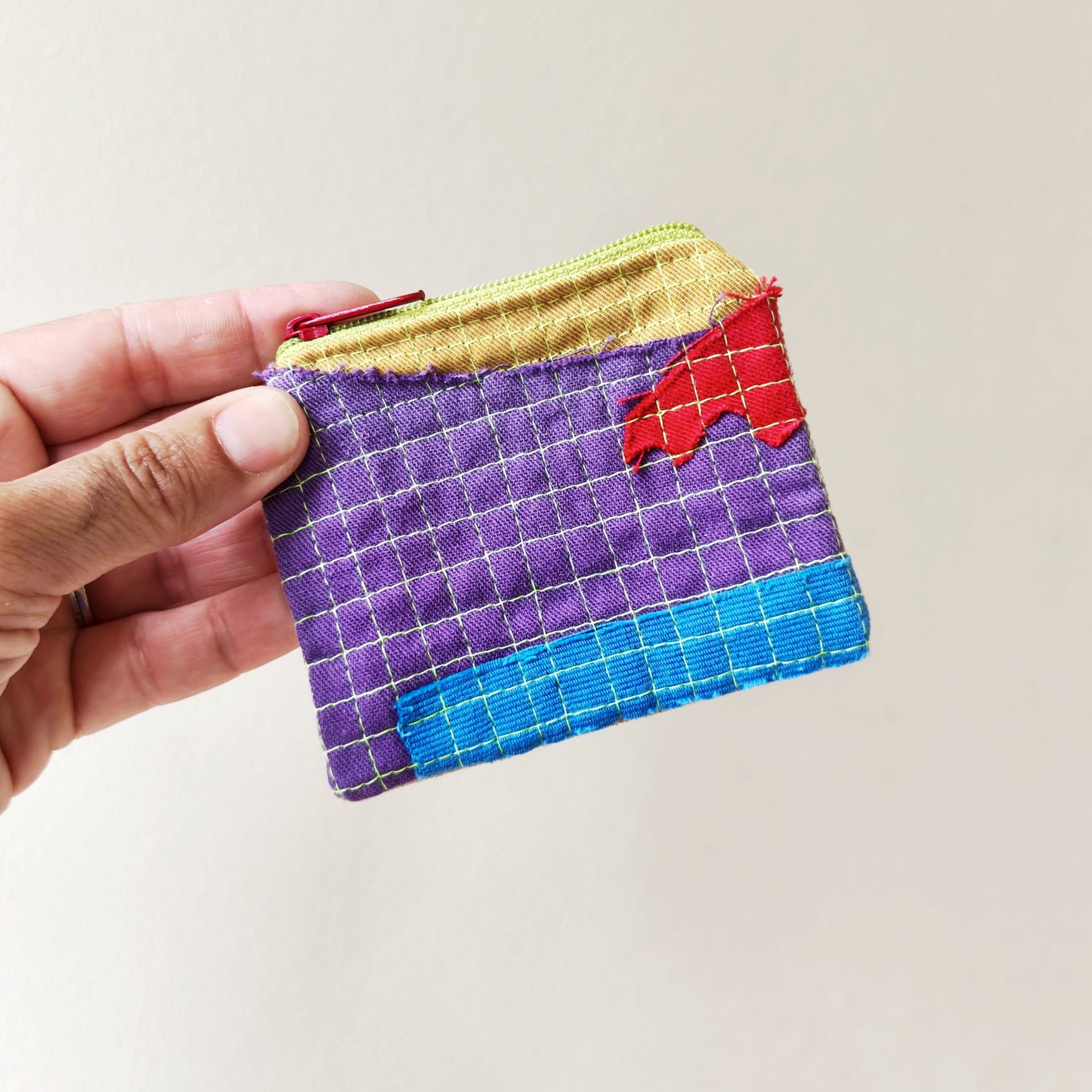 Mini bolsa trapo Carteira pequena colorida em tecido com fecho vermelho e costura verde, segurada por uma mão