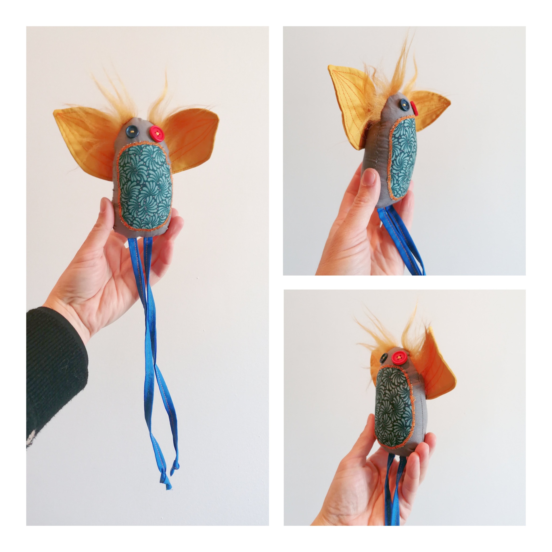 Passatortos! Figura decorativa artesanal com tecido azul-petróleo, orelhas laranja, olhos vermelhos e fitas azuis, segurada pela mão.