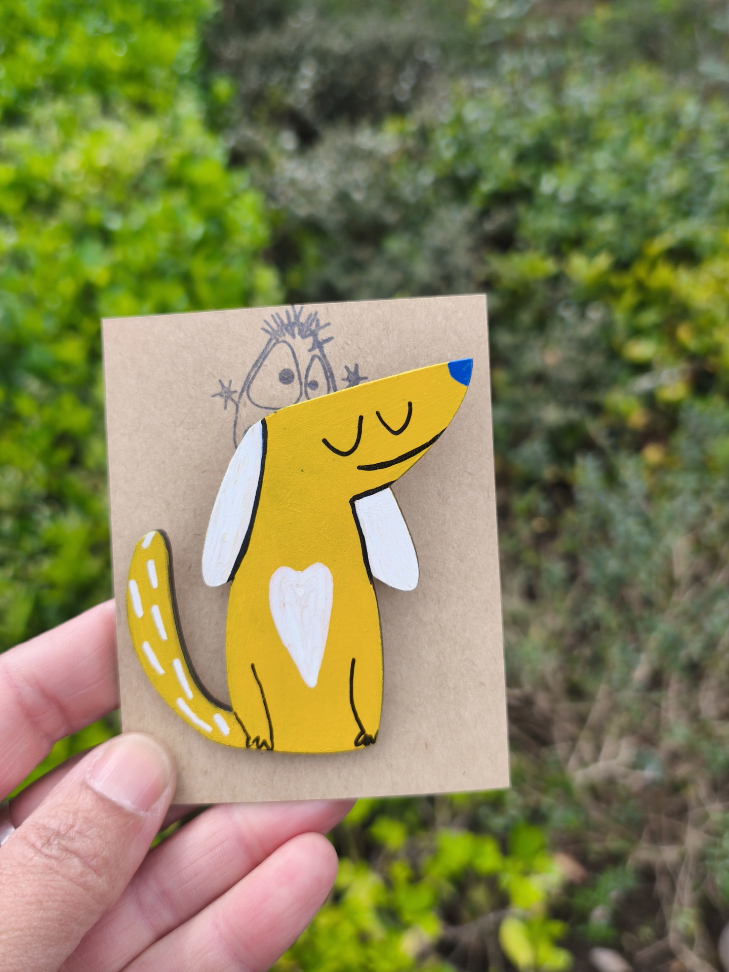 Alfinete cão! Broche de madeira pintada com desenho de cão amarelo e branco em fundo vegetal.