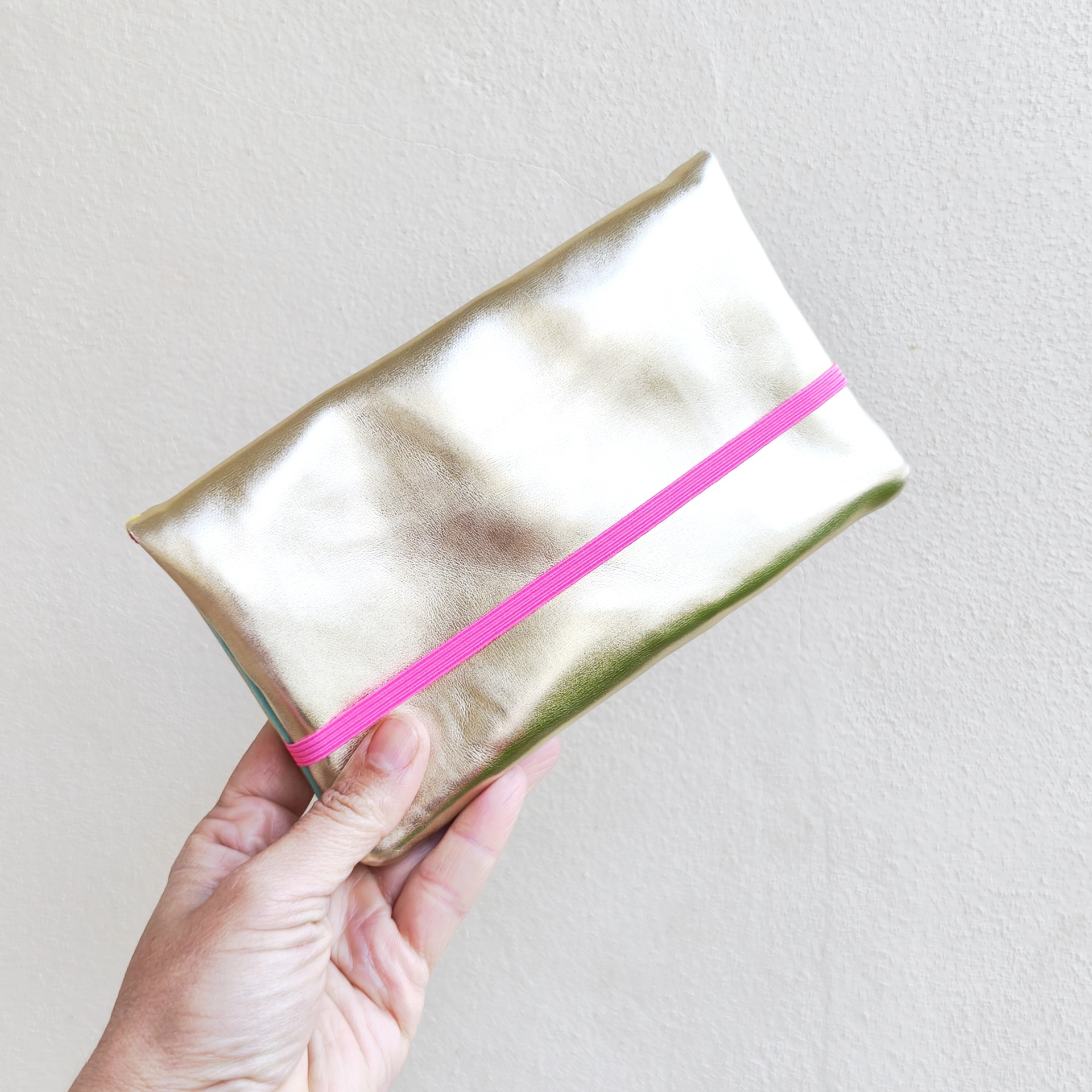 Carteiras porta-tudo! Estojo metálico dourado com elástico rosa segurado por uma mão