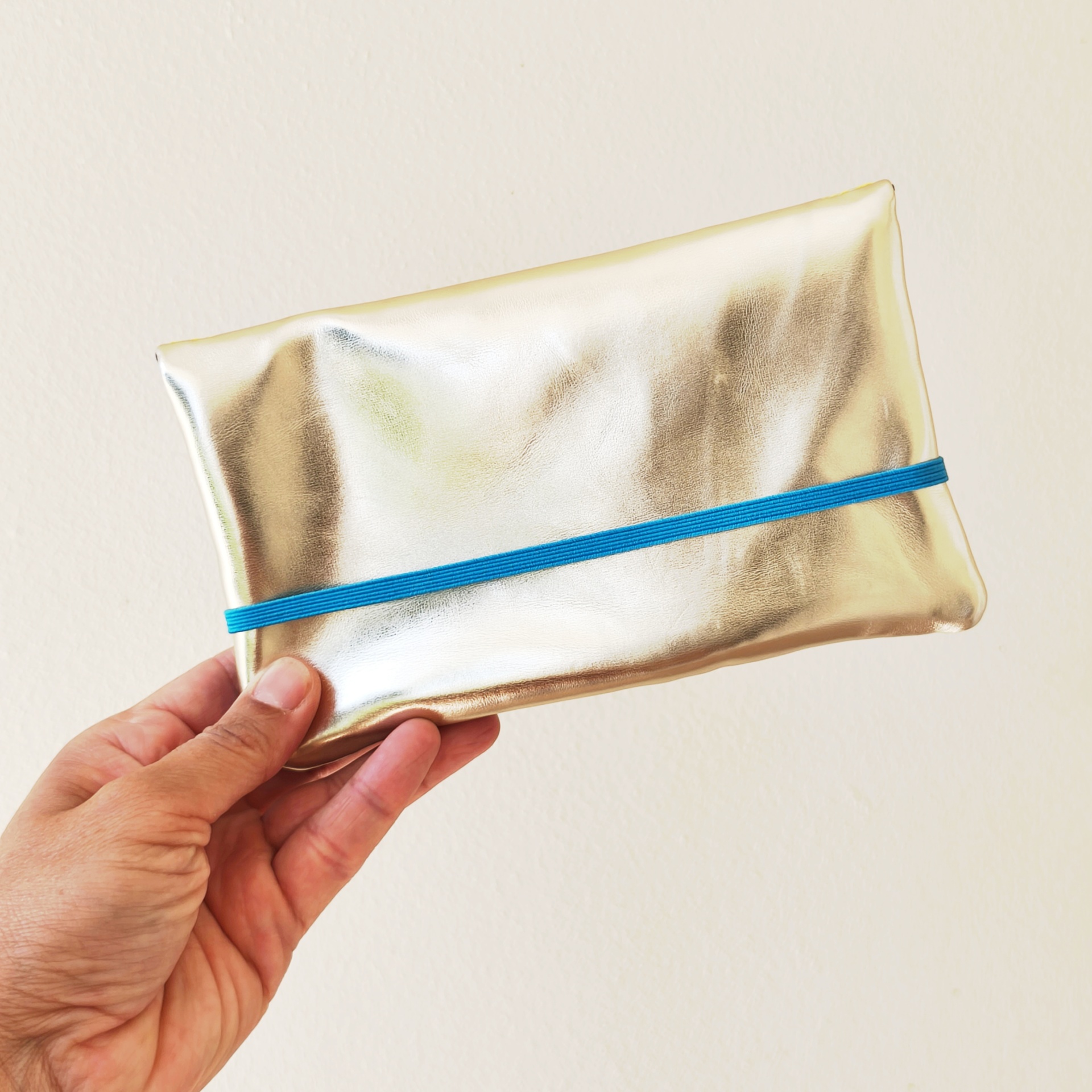 Carteiras porta-tudo! Estojo dourado com elástico azul segurado por mão