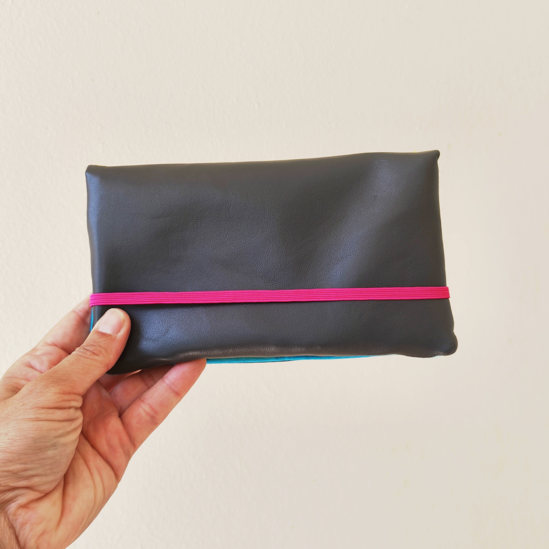 Carteiras porta-tudo! Carteira preta com elástico rosa vibrante, segurada por mão.