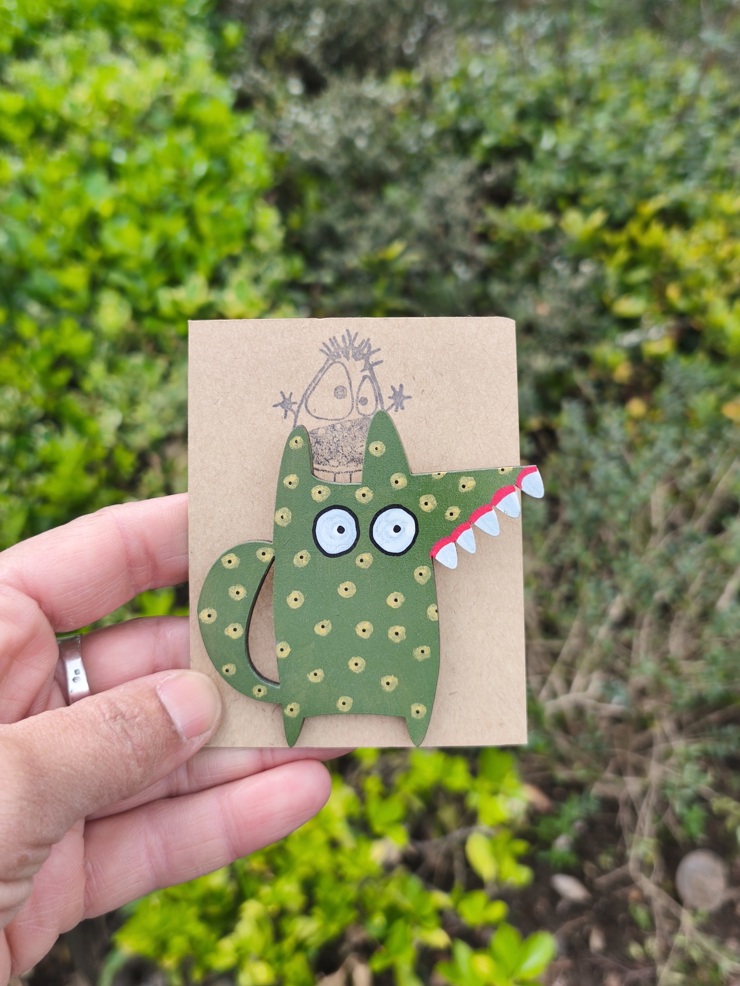 Alfinete lobo! Broche verde com pontos amarelos e dentes brancos em cartão castanho claro