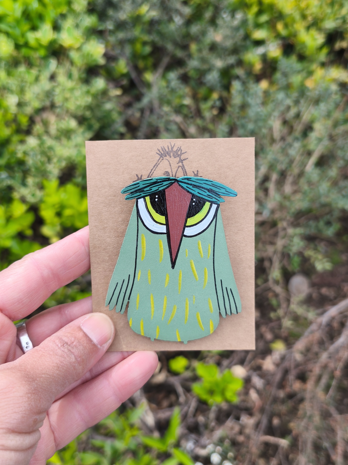 Alfinete mocho! Pin de pássaro verde com bico vermelho e sobrancelhas azuis num cartão castanho