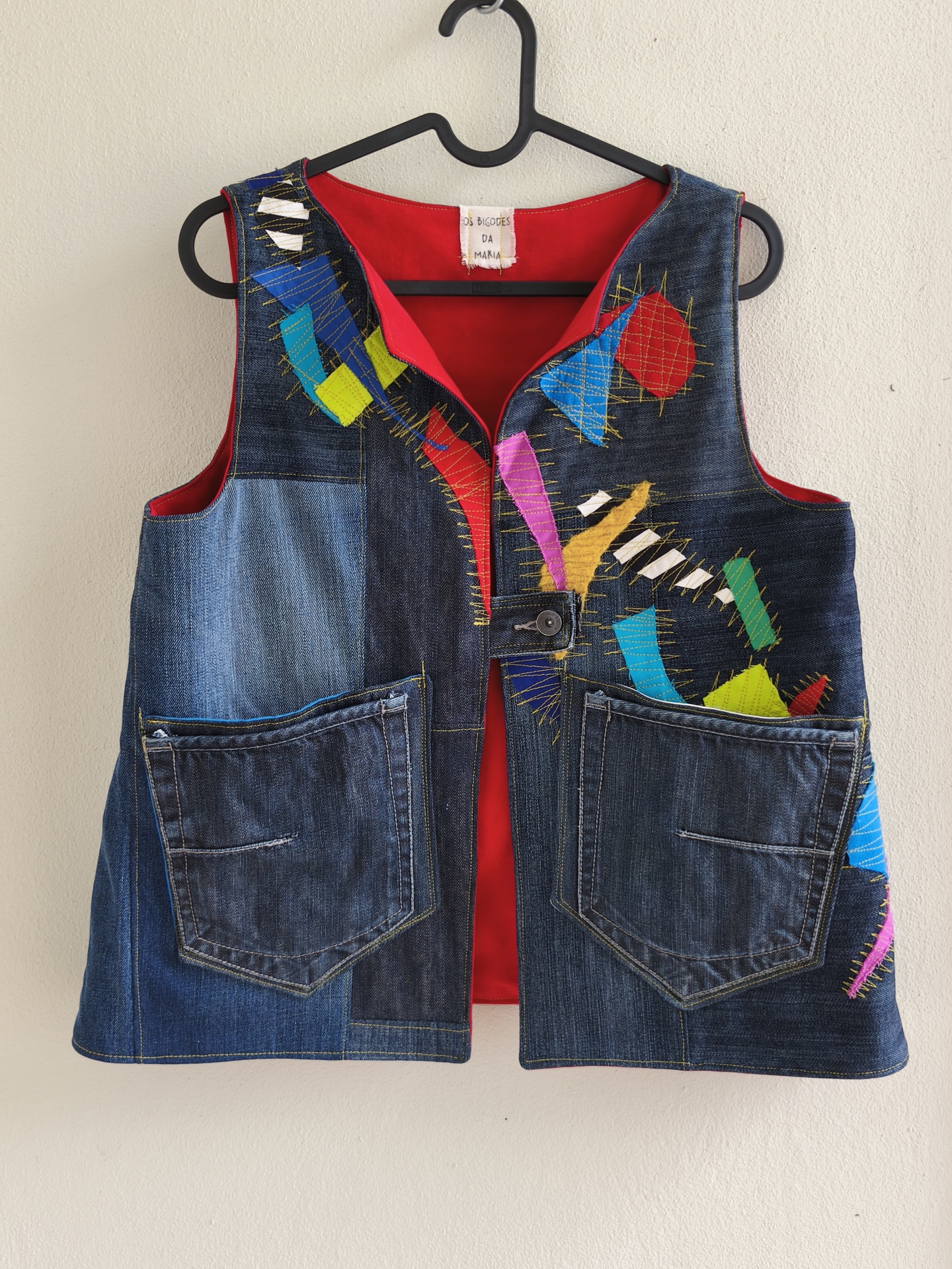 Coletes Trapo! Colete de jeans com remendos coloridos e interior vermelho pendurado em cabide