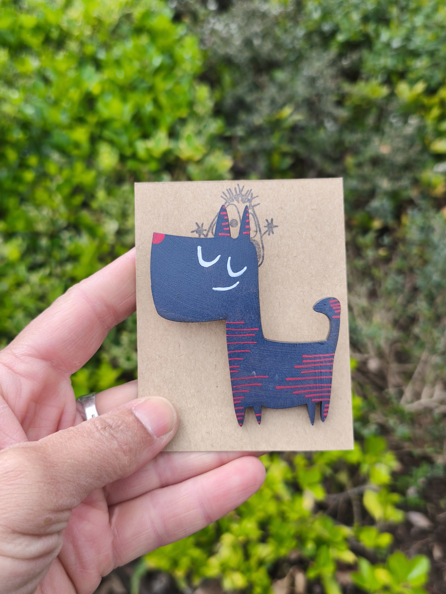 Alfinete cão #2! Broche azul escuro com linhas vermelhas em forma de cão, sobre cartão castanho