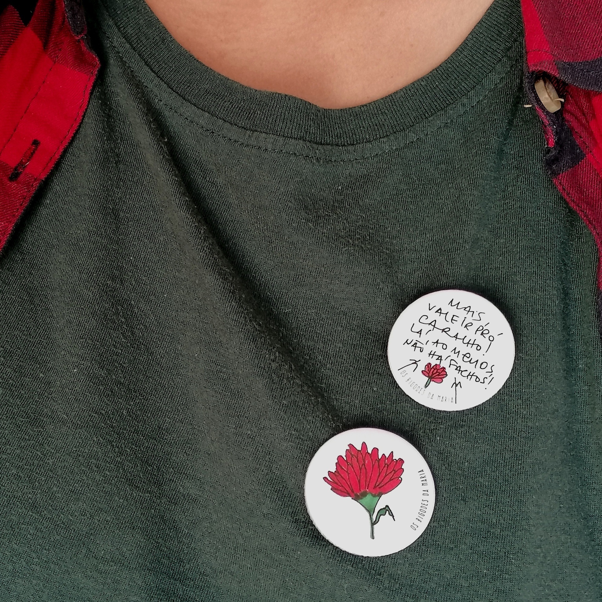 Pins anti-facho! Dois botons redondos com flor vermelha e texto manuscrito em t-shirt verde-escura