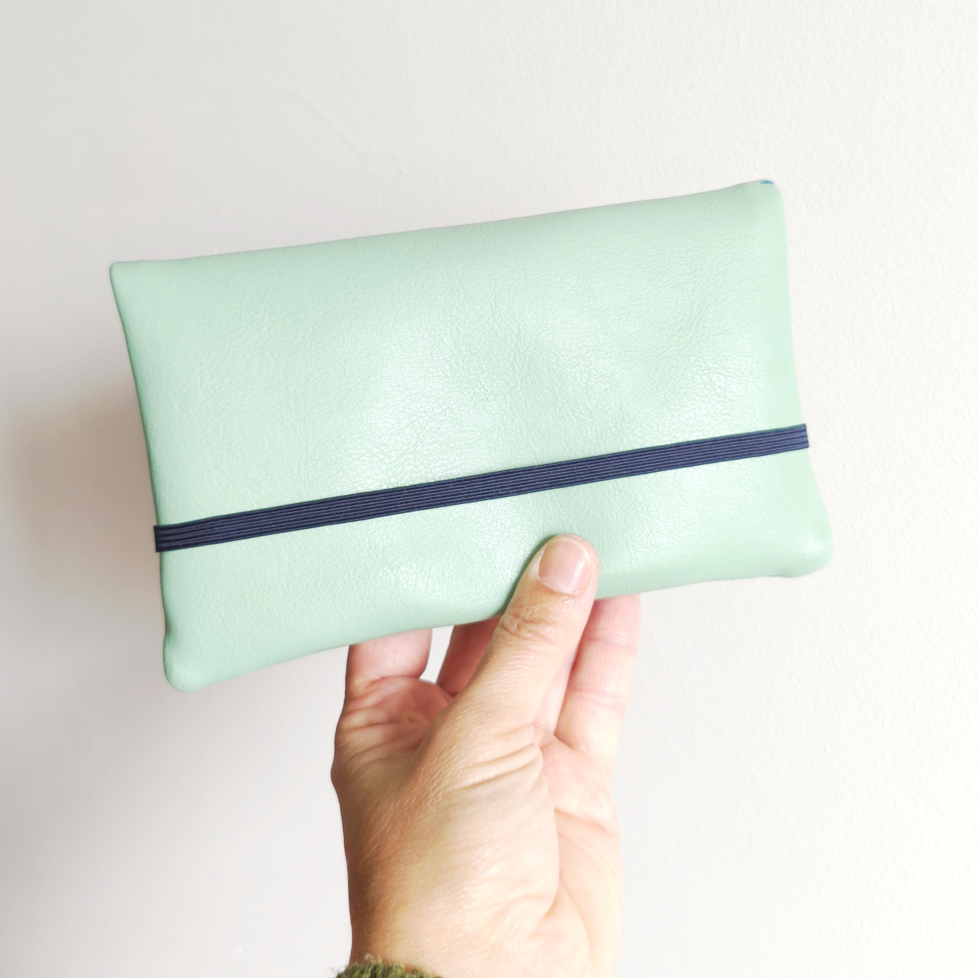 Carteiras porta-tudo! Carteira verde menta de couro com elástico preto segurada por mão
