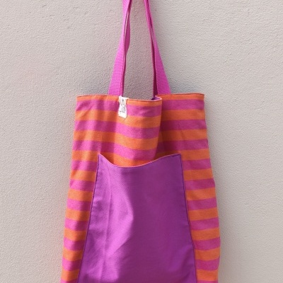 Saco listrado rosa e laranja com bolso rosa pendurado numa parede