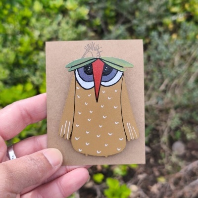 Broche coruja castanha com bico vermelho e folhas verdes na cabeça