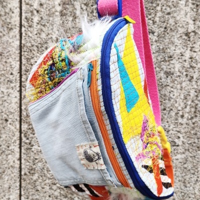 Mochila pequena colorida com padrão de rede e alça rosa pendurada em parede de pedra