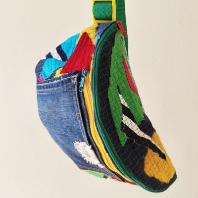 Bolsa colorida feita com retalhos de tecido e ganga com zíperes e alça verde pendurada numa parede branca